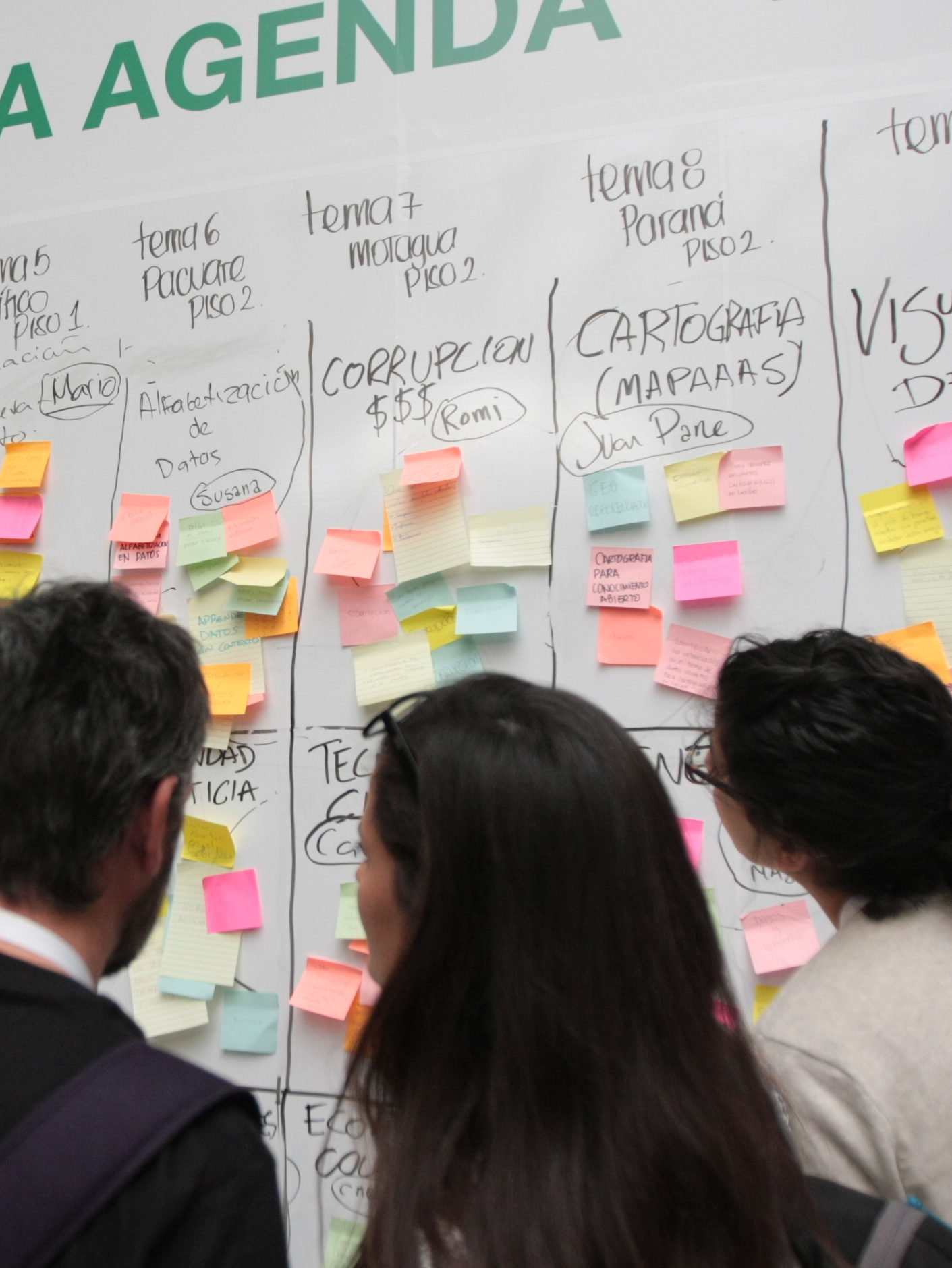 Un hombre y dos mujeres colocan notas adhesivas en el panel de construcción de agenda de ABRELATAM 2016 en Colombia.